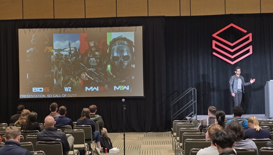 Speaker on stage beside a Databricks logo, presenting to a seated audience with Call of Duty key art on the projection screen